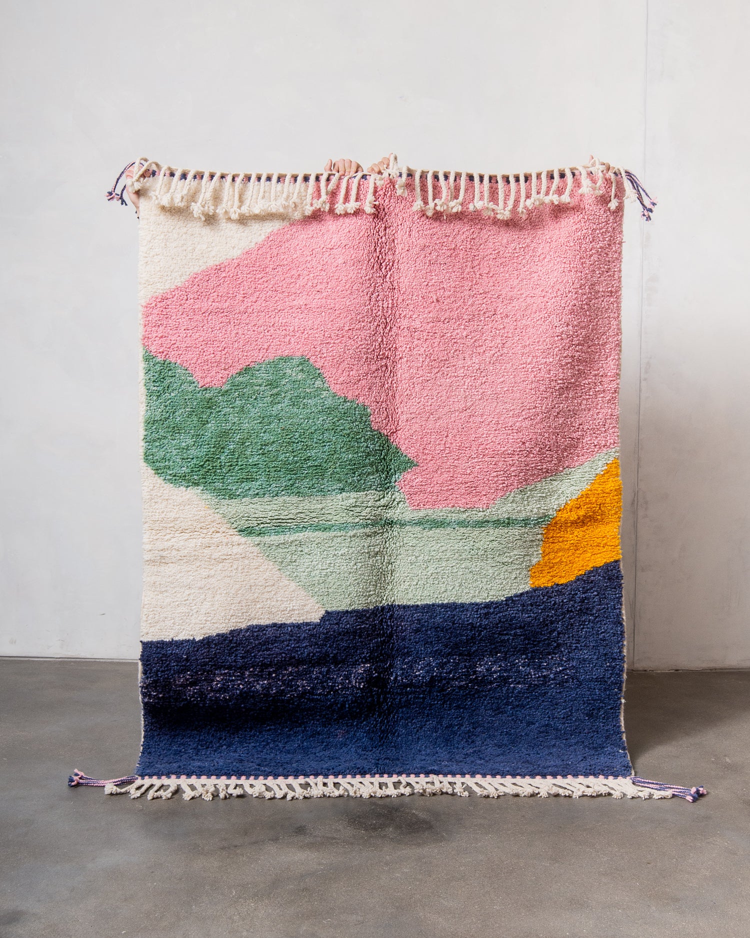 Berberlin Beniourain rug made of colourful wool, being held up in front of a white wall.